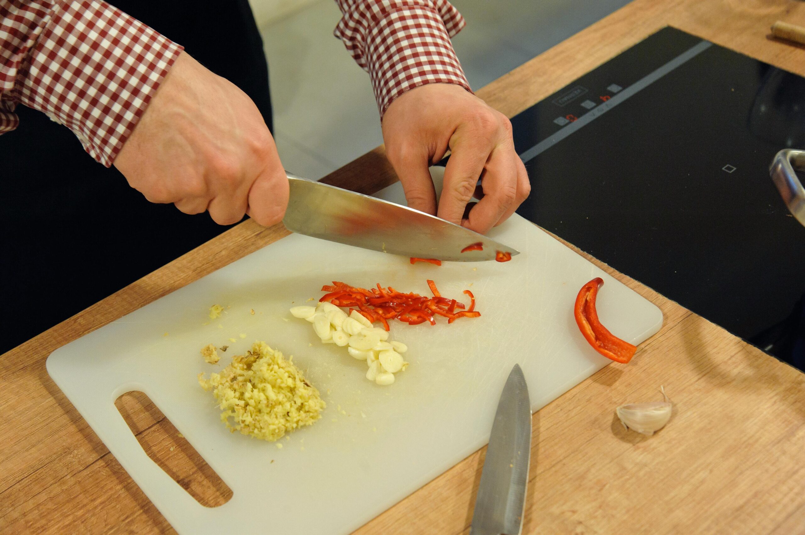 Garlic Chutney and Red Chilly Chutney Benefits: Why They’re Good for Health Close-up of hands chopping garlic and chili on a cutting board in a kitchen setting.