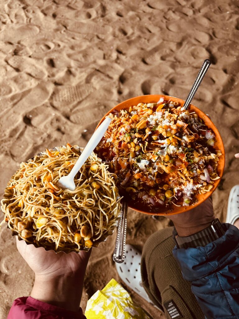 pexels photo 35113190 35113190 Vibrant street food bowls of chaat and noodles held over sandy beach in Puri, India.